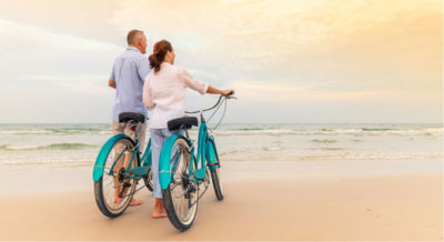Man and woman holding on their bicycles by the beach
